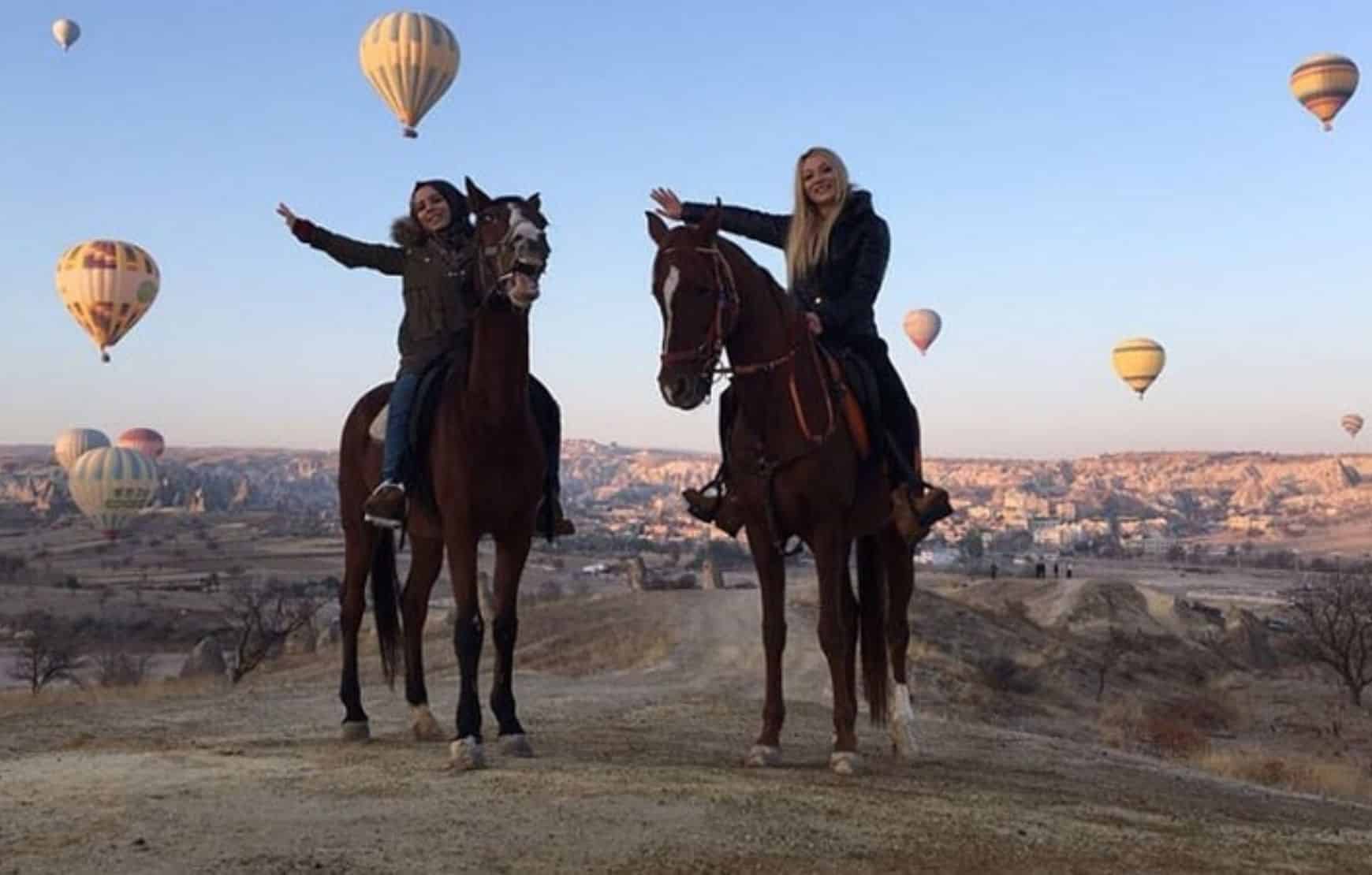 Horse Riding in Cappadocia - happy couple horseback riding in the morning with hot air balloon view
